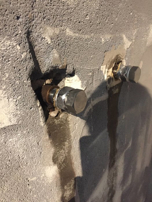 Två gamla duschanslutningskopplingar med speciellt mönster inmurade i en grå betongvägg.