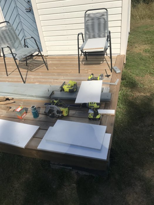 Arbetsverktyg och skivor på träbord för hantverksprojekt utomhus på en veranda.