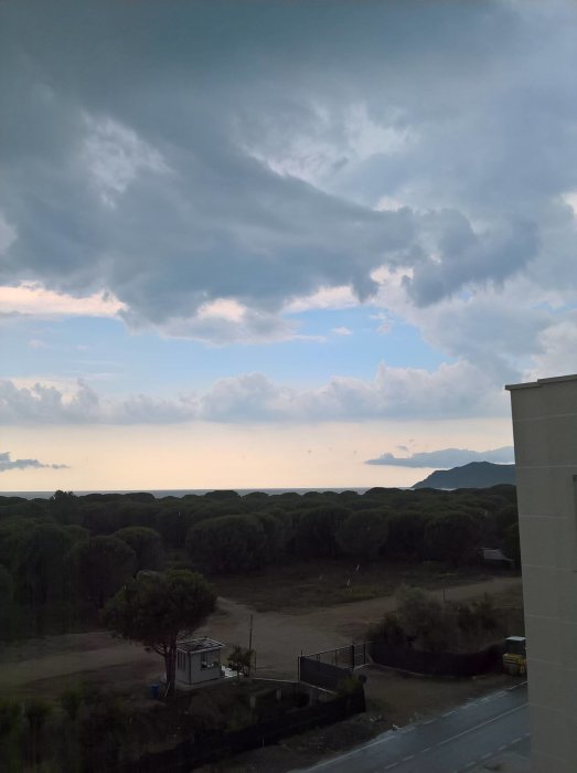 Mörka moln närmar sig över en landsby med berg i bakgrunden, hotfull himmel.