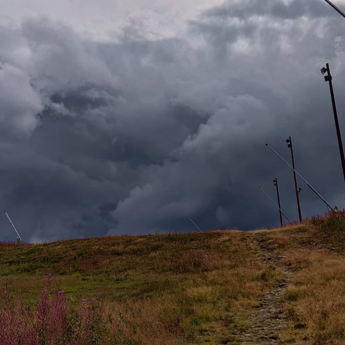 En stig på Lindvallen med mörka moln och skidliftstolpar i bakgrunden.