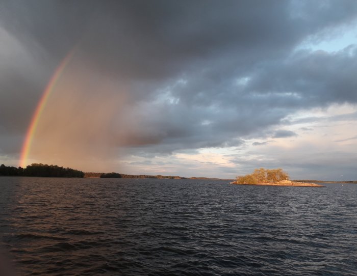 Regnbåge över en sjö med mörka moln och solbelyst ö på en fisketur.