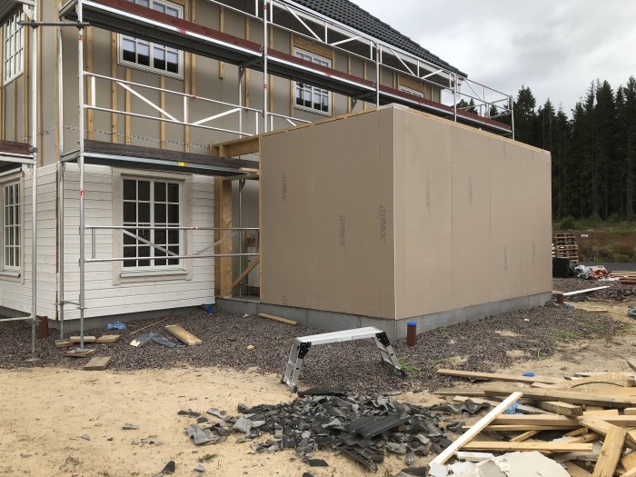 Hus under renovering med ställning och nypanelat uterum, byggnadsmaterial på marken.