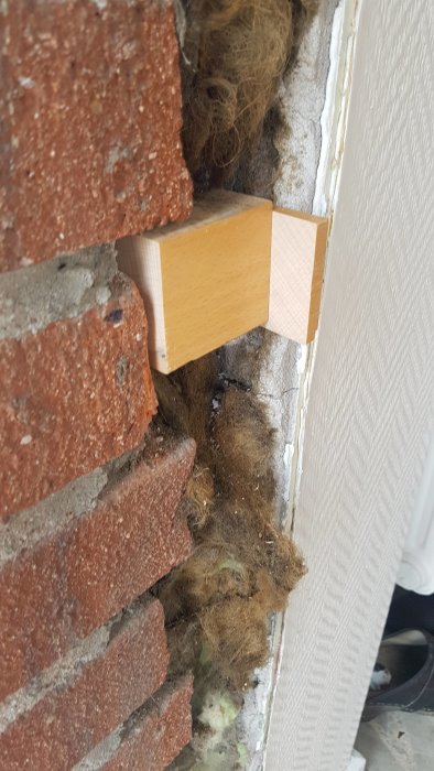 Ny träkil insatt mellan tegelsten och vit karm för att stabilisera en vägg.