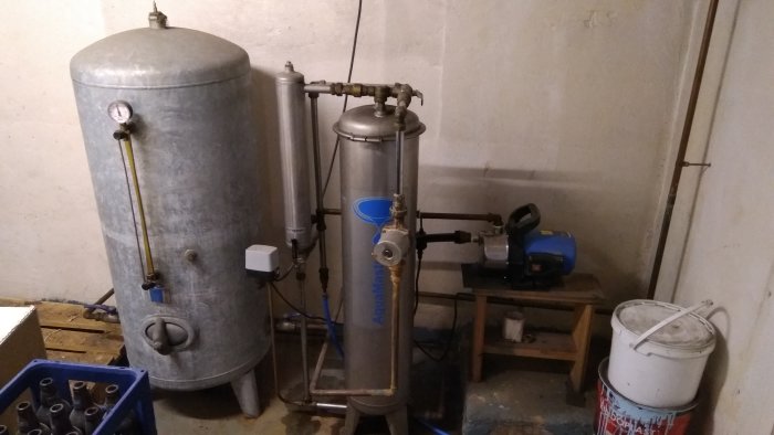 Vattenpump och trycktank i källare med anslutna rör och vattenfilter.
