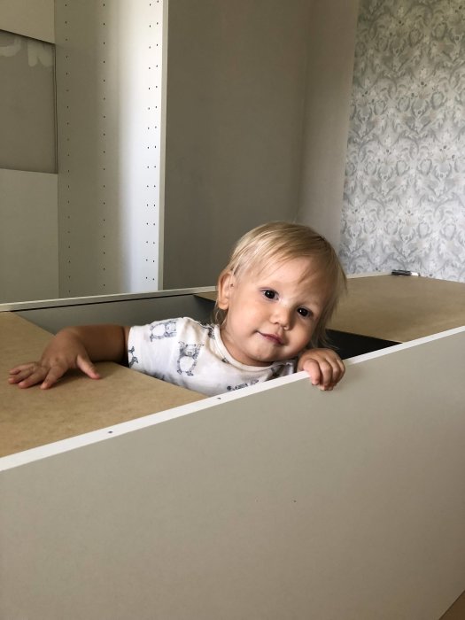 Litet barn som tittar fram genom ouppbyggd möbel under en hemma-snickarprojekt.