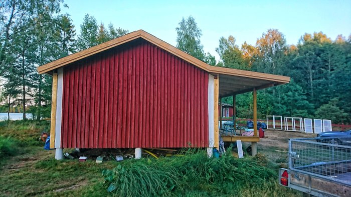 Ny målad röd vägg med takutstick och tillfälligt borttagna vita foderbrädor på ett hus under konstruktion.