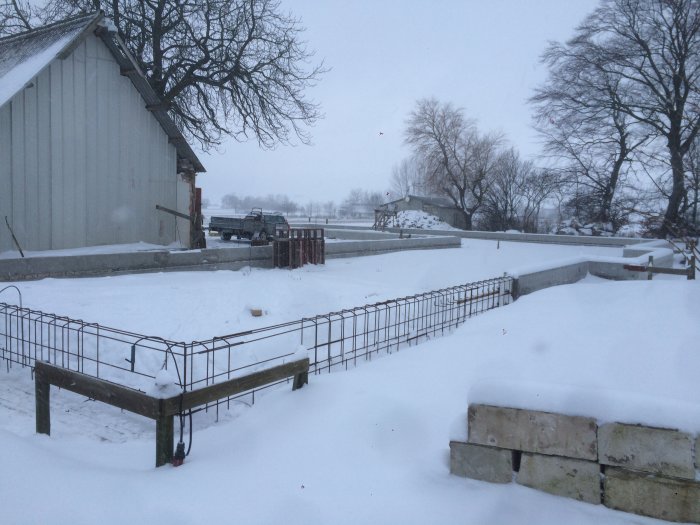 Nyformgjuten grund i sektioner täckt av snö med byggnad och träd i bakgrunden.