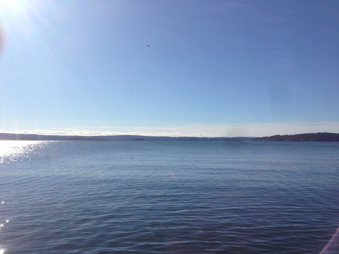 Stilla vatten i Oslofjorden med klar himmel och solstrålar som reflekterar på vattnet.