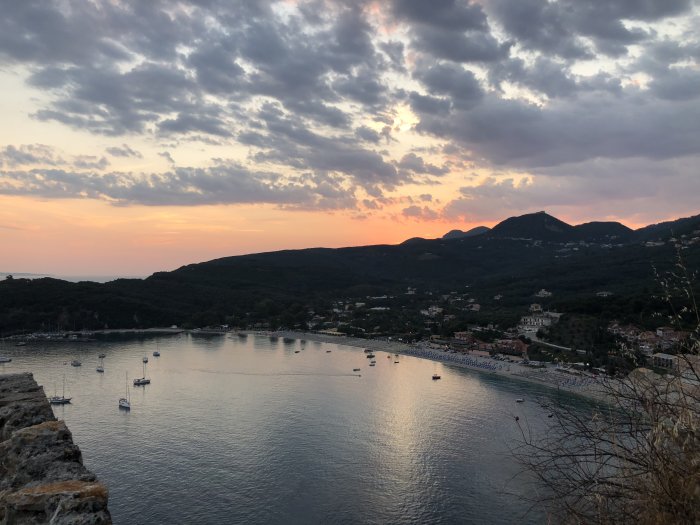 Solnedgång över en bukt med båtar i Parga, omgivet av berg och bebyggelse.