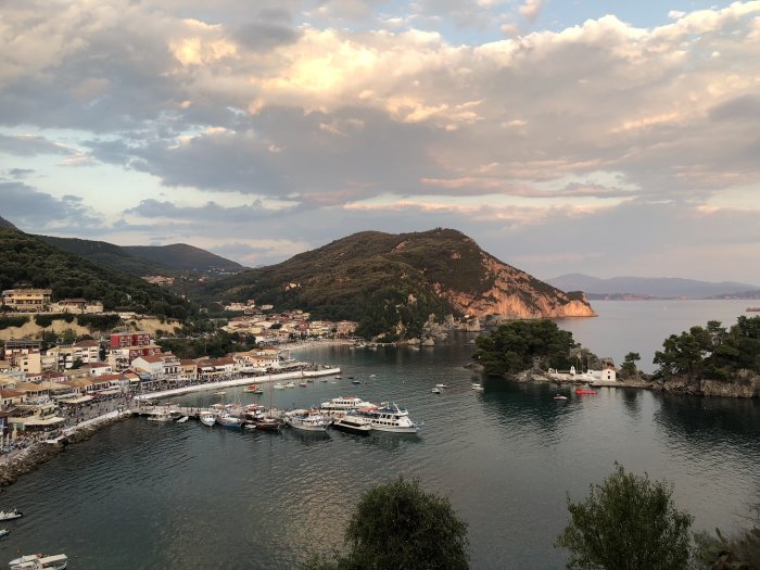 Vy över hamnen i Parga med båtar, byggnader och berg vid solnedgång.
