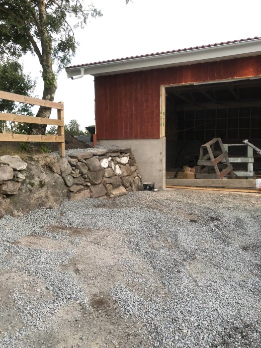 Grusad yta för blivande hundgård med stenmur och röd trägarage i bakgrunden.