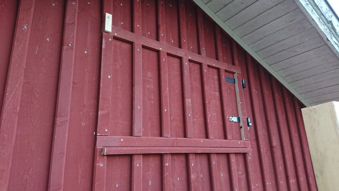 Renoverad vindslucka på rödmålad vägg under pågående exteriör snickararbete.