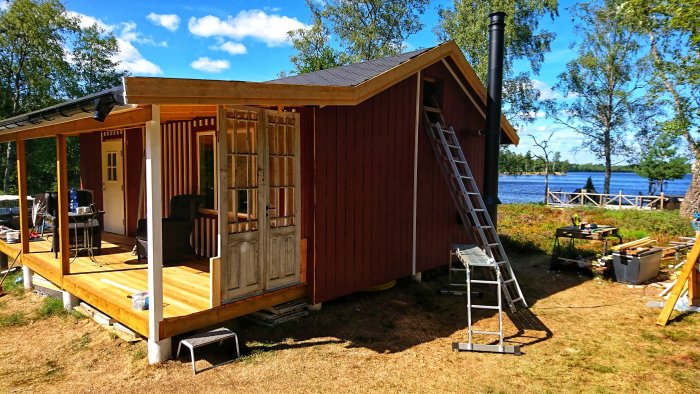 Träveranda under renovering med gamla pardörrar, verktyg och utsikt över vatten.