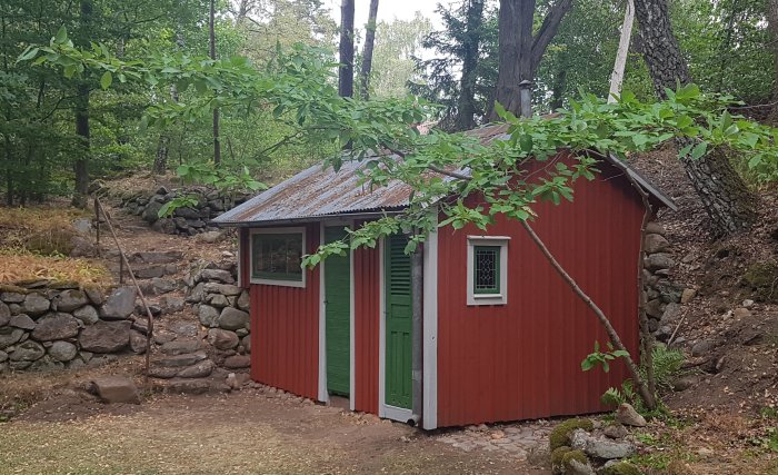 Nyinstallerat fönster i en röd stuga med vita knutar och gröna luckor i en skogsmiljö.