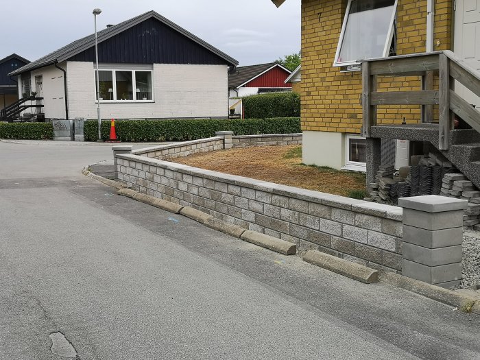 Renoverat stödmur i trädgården med makadam, fiberduk och stenblock, nära hus med växter.