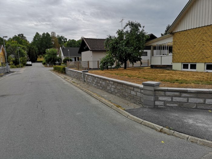 Nylagd stödmur av stenblock framför ett hus längs en asfalterad gata.