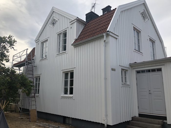 Renoverat hus med ställning på södersidan och nymålad källardörr.