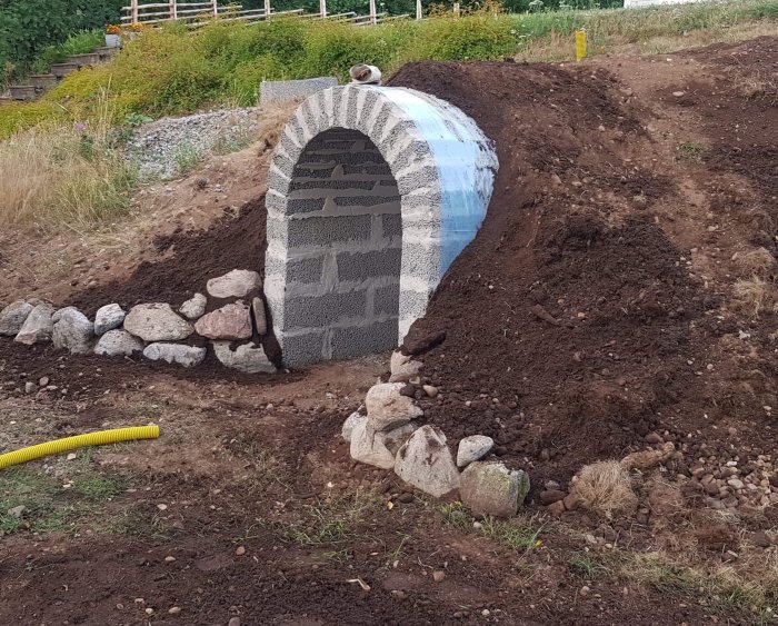 Halvfärdigt byggprojekt med borttagen form, oputsad framsida och jordhögar runt en konstruktion som liknar en grotta.