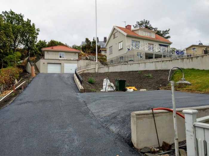 Nybelagd uppfart med asfalt framför villagarage, trädgård och hus i bakgrunden.