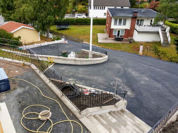 Nyligen asfalterad uppfart och trottoar med stenmur och trappor vid ett bostadshus.