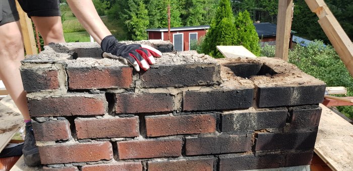 Person i arbetskläder håller i en delvis rivningsklar tegelskorsten med synligt möglande bruk.