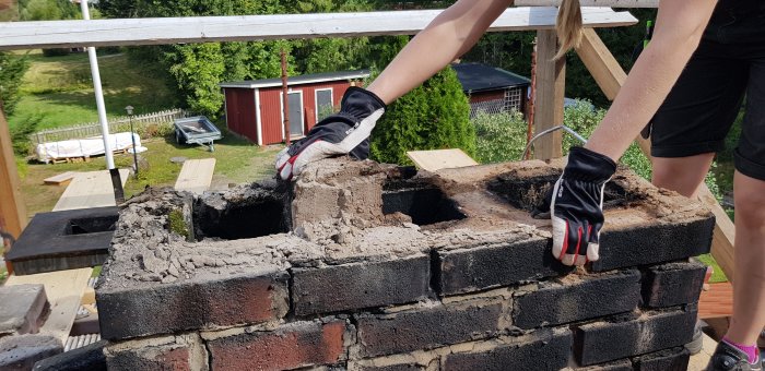 Person i arbetskläder och skyddshandskar demonterar en gammal skorsten byggd av tegelsten.