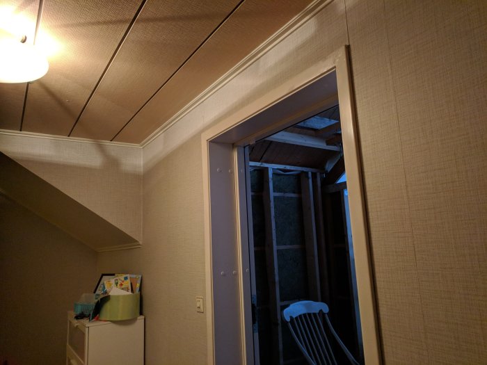 Bild på en öppen dörröppning som leder till ett ombyggnadsprojekt med synliga träreglar och takstomme.