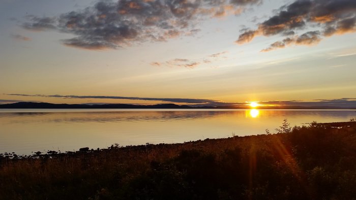 Solnedgång över Siljan med utsikt från båtklubbens klubbvik och gräsbevuxen strand.