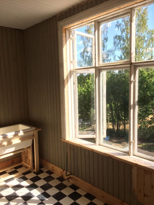 Renoverat rum med halvmålad vägg, schackrutigt golv och en träarbetsbänk vid ett fönster med utsikt.