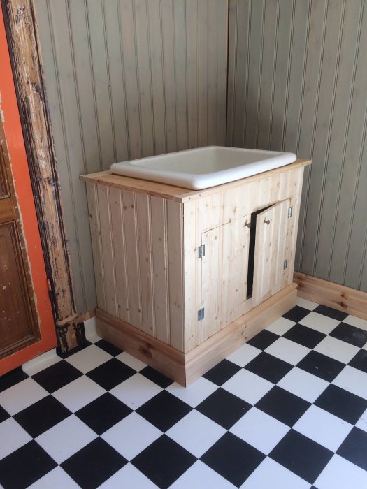 Renoverat badrum med ett nytt handgjort badrumsskåp och en ovanpåliggande tvättställ på ett golv med schackrutigt mönster.