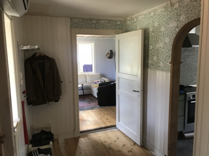 Inre hall i ett hem under renovering med trägolv, öppna vita dörrar och en bågformad dörröppning som leder till andra rum.