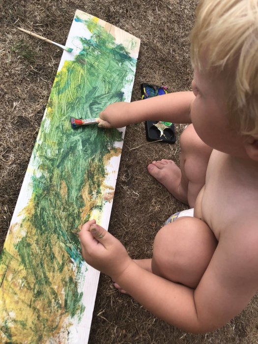 Barn målar kreativt på plank under en varm sommardag, "Team Junior" i arbete.