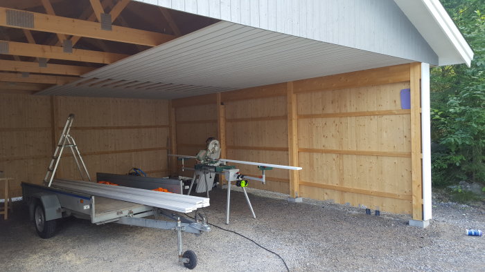 Halvt färdigställt innertak av vit panel, såg och byggmaterial i en carport under renovering.