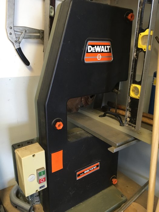 DeWalt bandsåg i verkstadsomgivning med justerbara styrningar och skyddshölje, modellnummer BS1310 synligt.