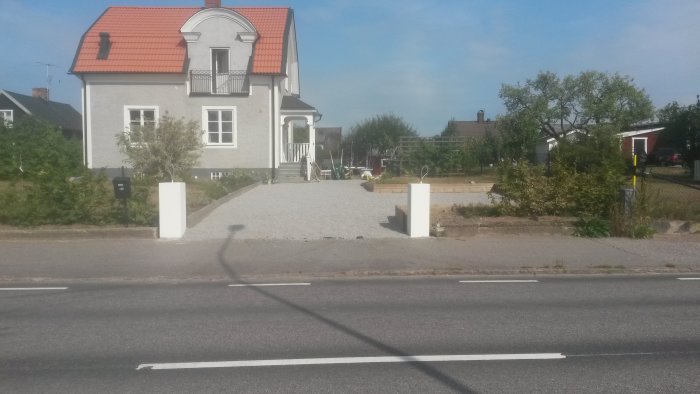 Vitmålade gjutna betongstolpar vid infart till hus med grusgång och postlåda.