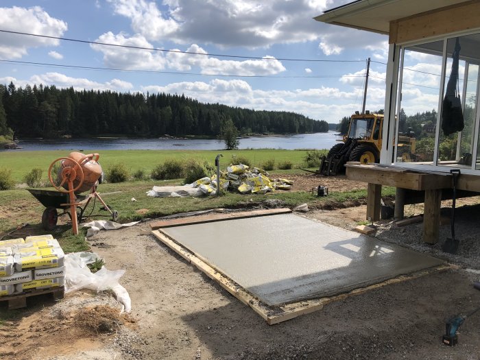 Ny gjuten betongplatta för jacuzzi bredvid altan med utsikt över Västerdalälvens forsar, byggmaterial och maskiner i förgrunden.