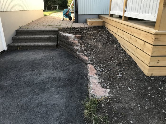 Gårdsplan intill trappa och altan före renovering; grävd rabattkant och altanens inklädnad syns.