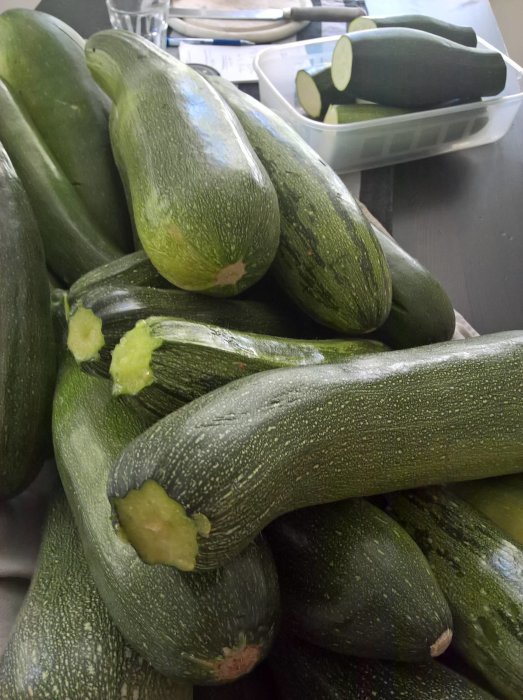 Stapel med hemodlade squash i olika storlekar, vissa halverade, på ett köksbord.