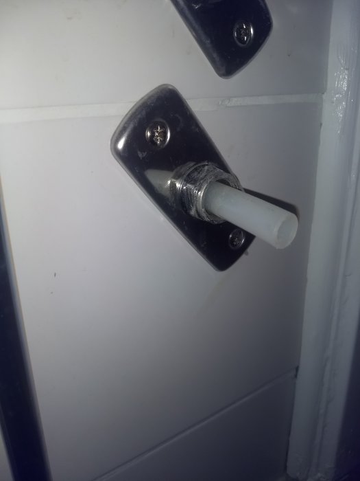 Närbild av en vit dörrstängare monterad på svart dörrplatta, synlig slitage och felsökning pågår.