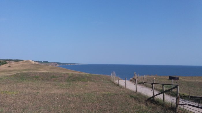 Utsikt över kustlandskap vid Sandhammaren med sanddyner, hav och klarblå himmel.