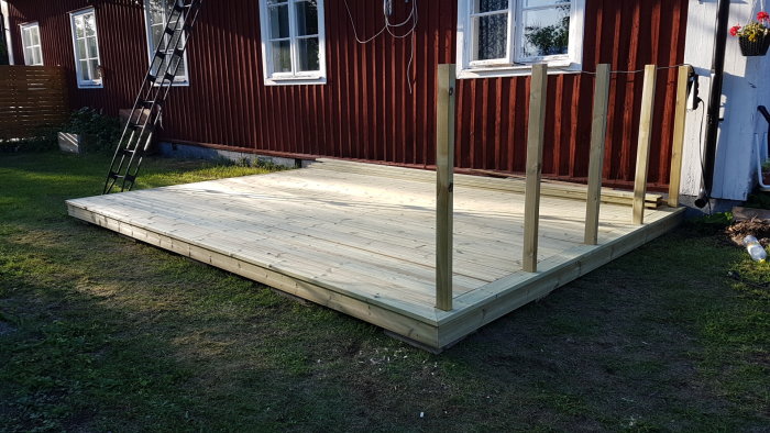 Nybyggd träuteplats utan spaljé vid ett rött hus, med pelare uppställda, klar för slutlig finish.