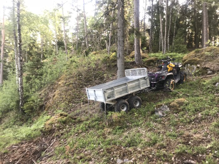 En ATV parkerad i skogsmark med ett kopplat släpvagn i en grön naturmiljö.