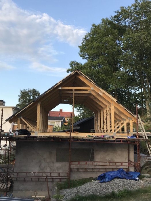 Trästomme till ett garage med loft under konstruktion och öppen takstol mot en klar himmel.