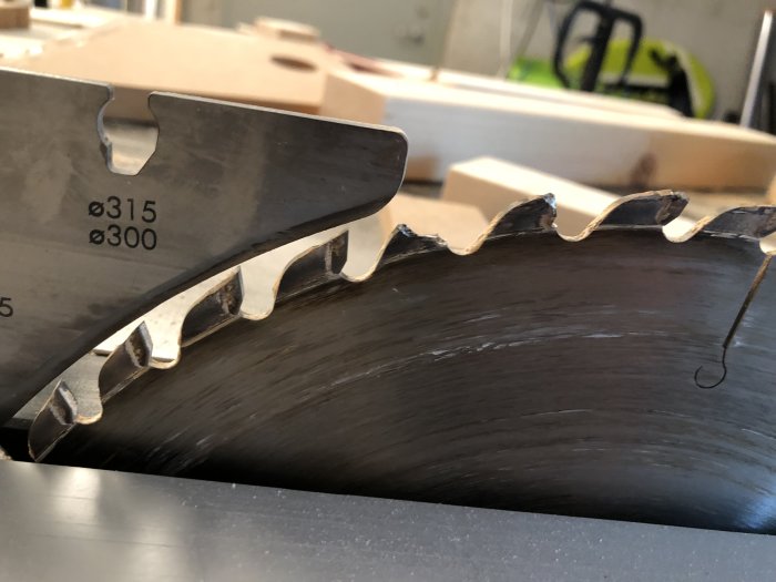 Närbild på en sågklinga utan skydd, med några träspån i verkstadsbakgrund.