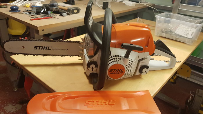 Knappast använd STIHL MS 251 C motorsåg på ett arbetsbord med verktyg i bakgrunden.