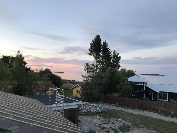 Utsikt över hav vid skymning från en byggarbetsplats med halvfärdigt tak och byggnadsställning.