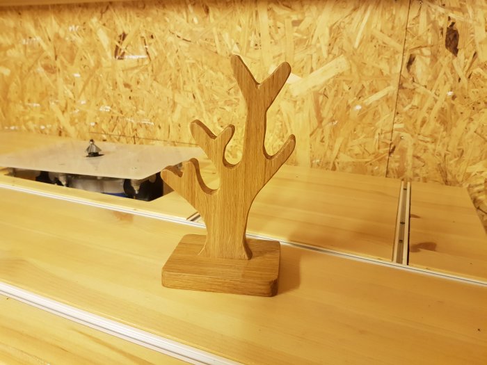 Handgjort trädsmyckesträd av ek placerat på en trähylla mot en spånskivevägg.