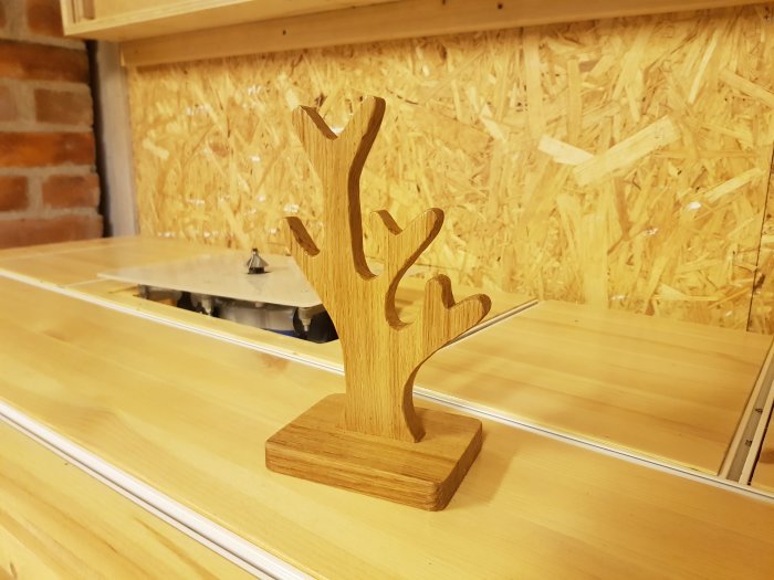 Hemgjort smyckesträd i ek placerat på en trähylla, används för att hänga ringar.