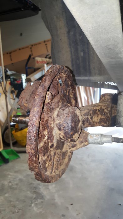 Bromsdel på släpvagn med synlig korrosion och skadad bromssköld i ett garage.