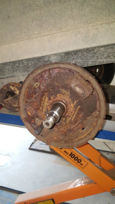 Rostig bromstrommel och axel från ett släp upplyft på ett mekaniskt lyftbord i ett garage.